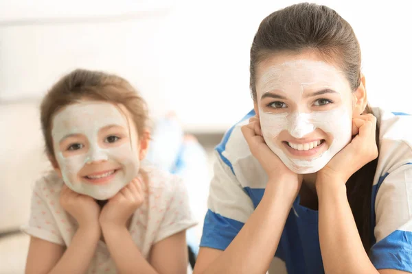 Young woman and her little daughter with facial masks at home — Stock Photo, Image
