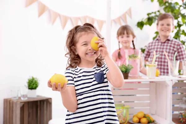 Niedliches kleines Mädchen mit Zitronen und verschwommenem Stand mit Kindern im Hintergrund — Stockfoto