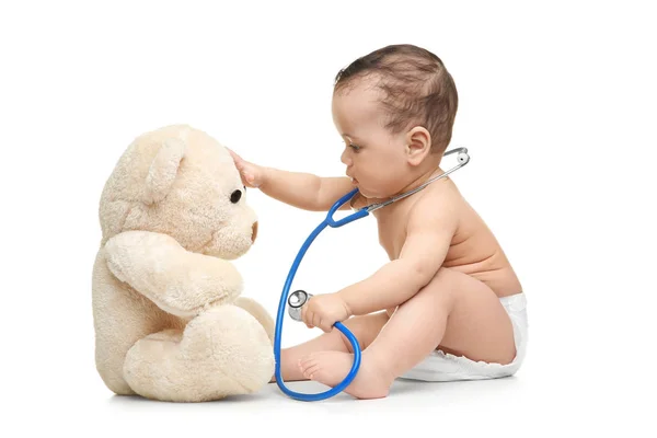 Bebê bonito brincando com estetoscópio e urso de brinquedo no fundo branco. Conceito de saúde — Fotografia de Stock