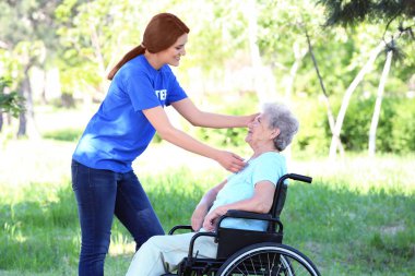 Genç kadın gönüllü açık havada ile tekerlekli sandalye üzerinde mutlu kadın kıdemli
