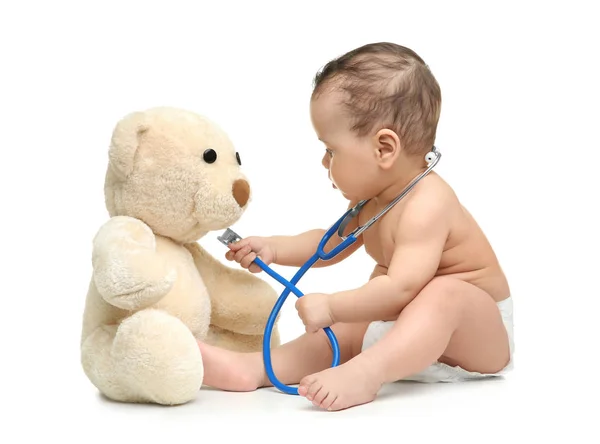 Niedliches kleines Baby, das mit Stethoskop und Spielzeugbär auf weißem Hintergrund spielt. Gesundheitskonzept — Stockfoto