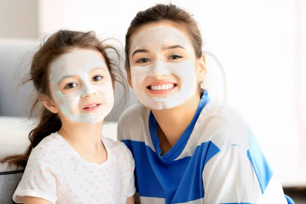 Młoda kobieta i jej córeczkę z twarzy maski w domu — Zdjęcie stockowe