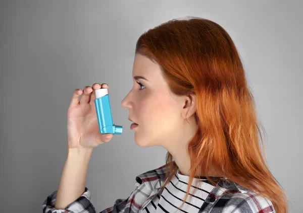 Jonge vrouw met behulp van de inhalator voor astma en ademhalingsaandoeningen op lichte achtergrond — Stockfoto