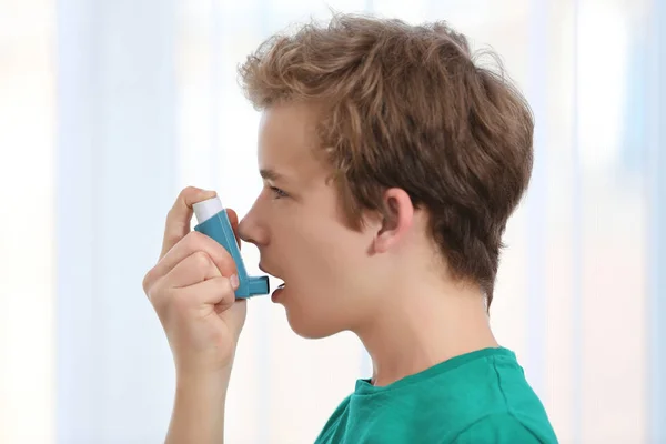 Menino usando inalador para asma e doenças respiratórias em fundo claro — Fotografia de Stock