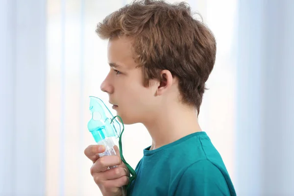 Mladý chlapec pomocí rozprašovač pro astma a onemocnění dýchacích cest na světlé pozadí — Stock fotografie
