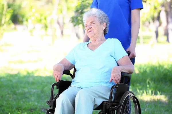 Gelukkig senior vrouw op rolstoel met jonge vrouwelijke vrijwilligers outdoors — Stockfoto