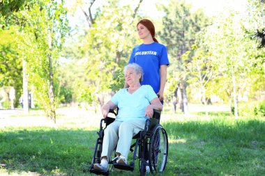 Genç kadın gönüllü açık havada ile tekerlekli sandalye üzerinde mutlu kadın kıdemli