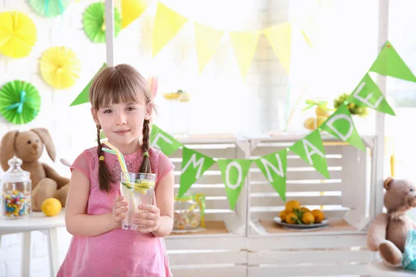 Милая маленькая девочка держит стекло и размытый стенд с лимонадом на заднем плане — стоковое фото