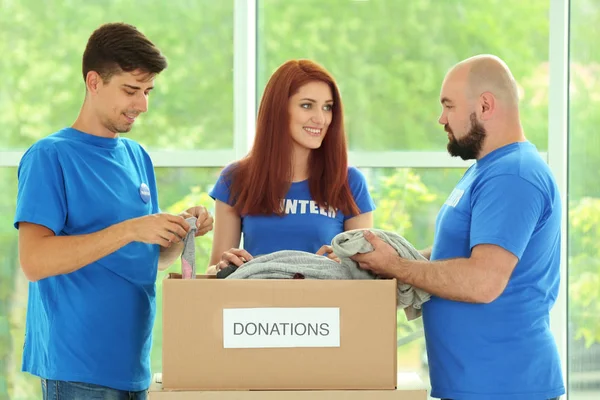 Young volunteers with box of donations indoors — Stock Photo, Image