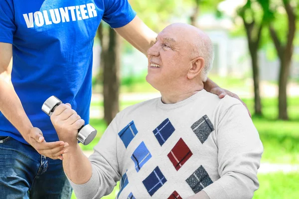 Молодий волонтер допомагає старшому чоловікові виконувати вправи з гантелі на відкритому повітрі — стокове фото