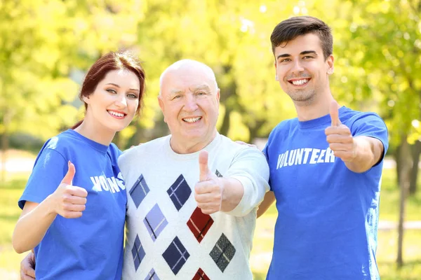 Feliz hombre mayor y jóvenes voluntarios al aire libre en el día soleado —  Fotos de Stock