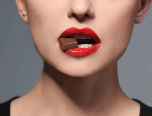 Vacker ung kvinna med ljusa läppar äta bit av choklad, närbild — Stockfoto