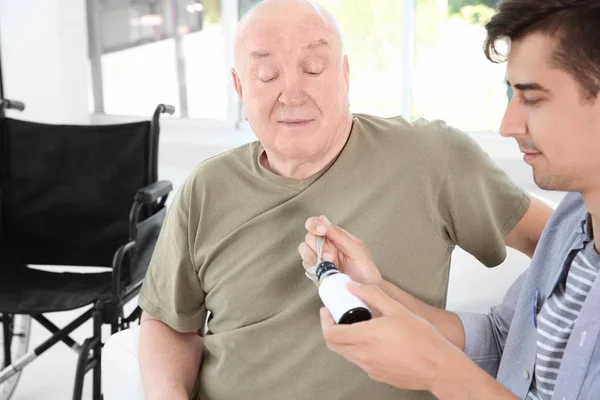 Jonge mannelijke vrijwilligers geven geneeskunde voor senior man in lichte kamer — Stockfoto