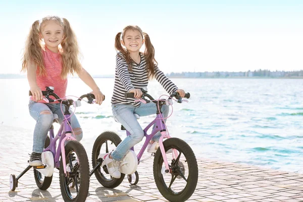 Meninas bonitos andar de bicicleta perto do rio no dia ensolarado — Fotografia de Stock