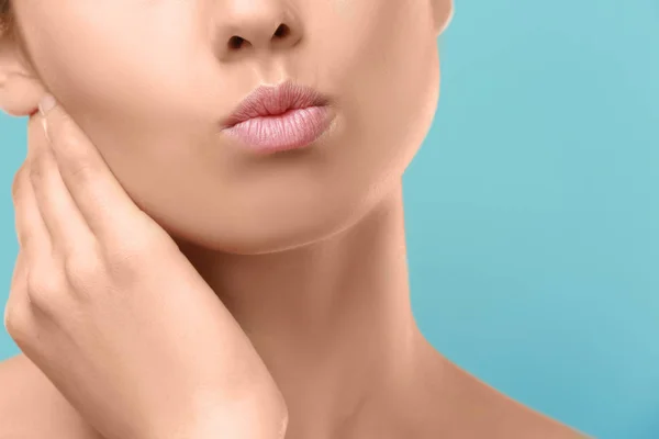 Vista de cerca de la hermosa mujer joven con labios naturales maquillaje tocando el cuello en el fondo de color — Foto de Stock