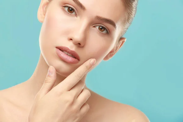 Nahaufnahme Ansicht der schönen jungen Frau mit natürlichen Lippen Make-up berühren Gesicht auf farbigem Hintergrund — Stockfoto