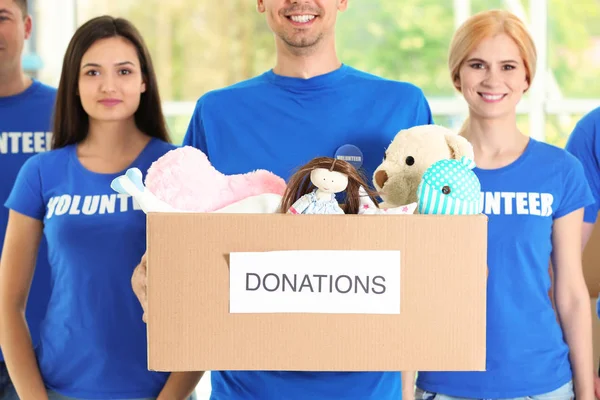 Young volunteers with box of donations indoors — Stock Photo, Image