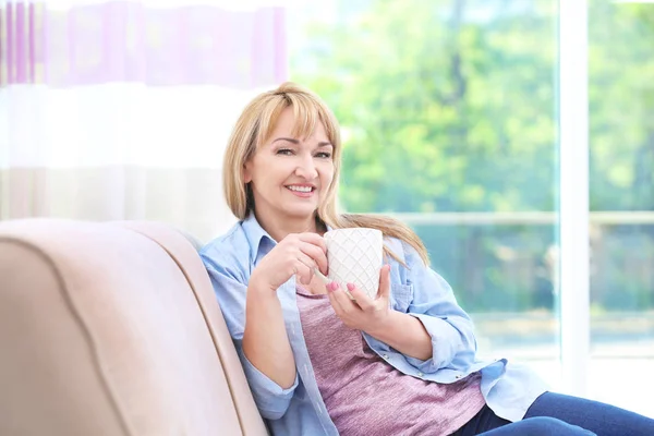 Atractiva mujer madura sonriente sentada en el sofá en casa — Foto de Stock