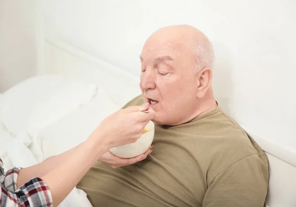 Joven voluntaria alimentando a anciano en interiores — Foto de Stock