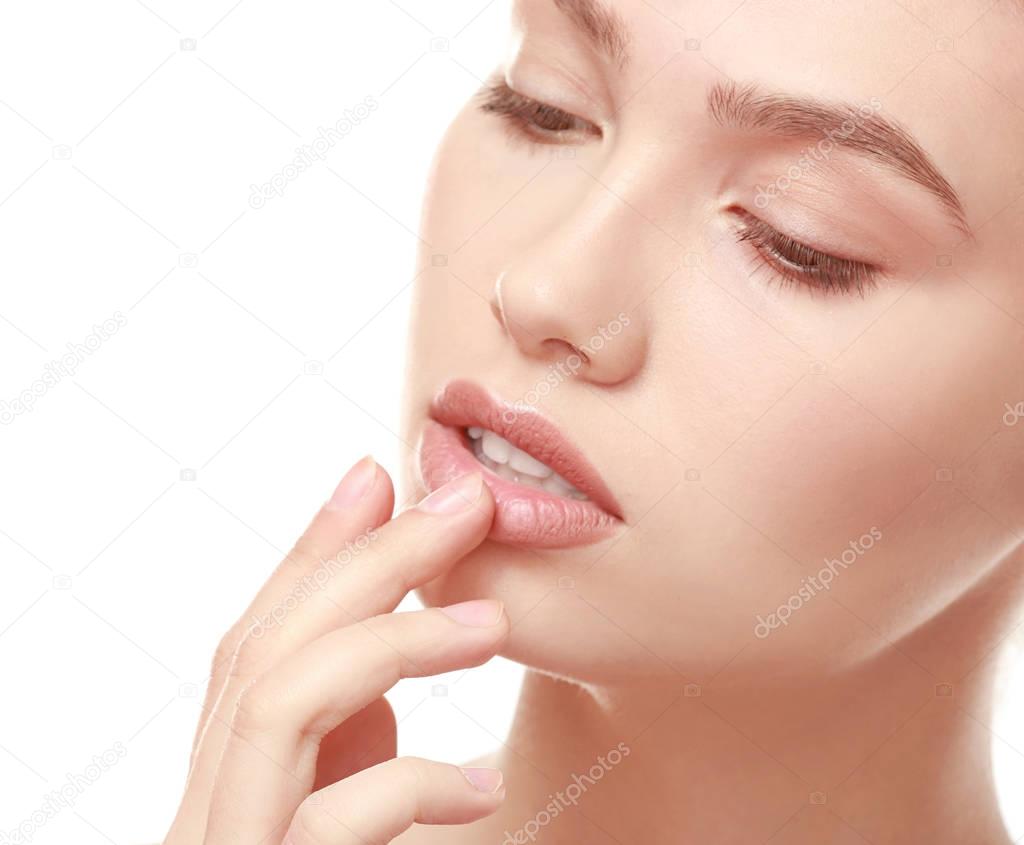 Closeup view of beautiful young woman with natural makeup touching lips on white background