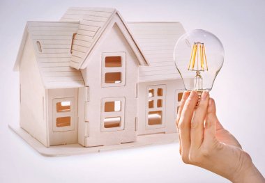 Ampul ve evin arka plan üzerinde model tutan kadın. Enerji tüketimi kavramı