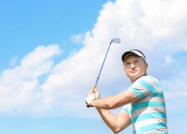Genç adam golf kursunda güneşli bir günde oynuyor.