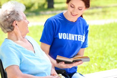 Genç kadın gönüllü okuma kitap kadın kıdemli için tekerlekli sandalye açık havada