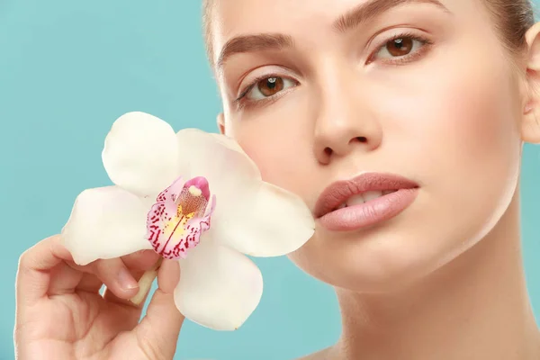 Vista de cerca de la hermosa mujer joven con maquillaje de labios naturales y flor en el fondo de color —  Fotos de Stock