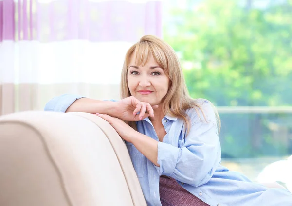 Ελκυστικό χαμόγελο ώριμη γυναίκα που κάθεται στον καναπέ στο σπίτι — Φωτογραφία Αρχείου