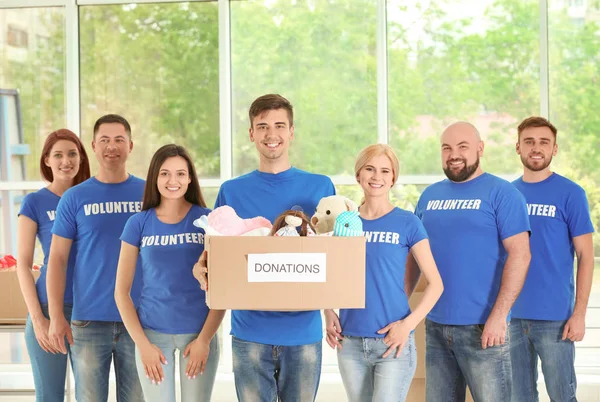 Young volunteers with box of donations indoors — Stock Photo, Image