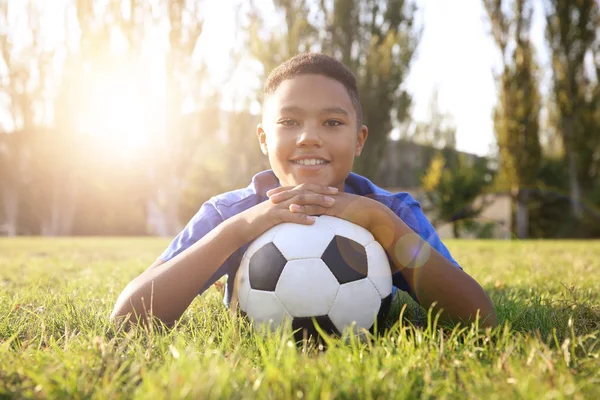 Afro-Amerikaanse jongen met voetbal liggend op groen gras in park. Voetbal concept — Stockfoto