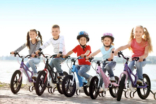 Cute little children riding bicycles near river on sunny day — Stock Photo, Image