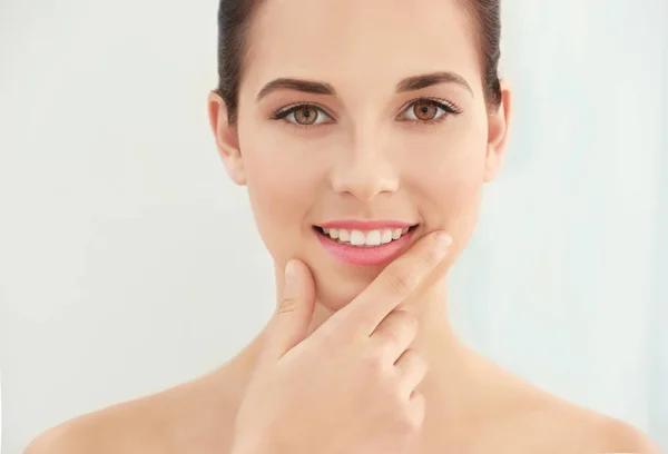 Vista de cerca de la hermosa mujer joven con labios naturales maquillaje tocando la cara en el fondo claro — Foto de Stock