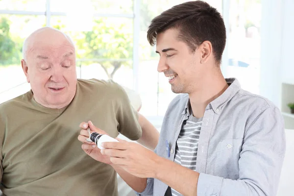 Young male volunteer giving medicine to senior man in light room — Stock Photo, Image