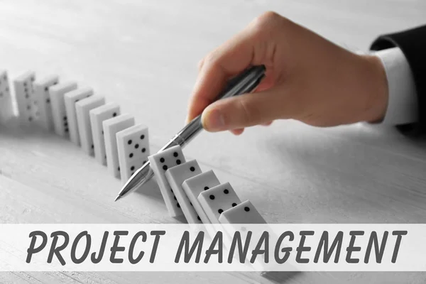 Koncepcja zarządzania projektami. Człowiek próbuje zatrzymać spadające Domino na podłoże drewniane — Zdjęcie stockowe