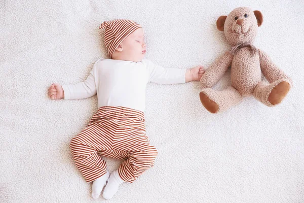 Niedliches kleines Baby mit Spielzeugbär schläft auf Plaid zu Hause — Stockfoto