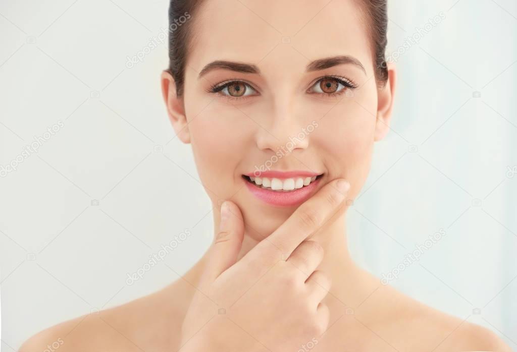 Closeup view of beautiful young woman with natural lips makeup touching face on light background