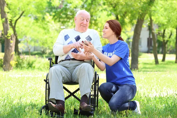 Jonge vrouwelijke vrijwilligers en senior man op rolstoel met mobiele telefoon outdoors — Stockfoto