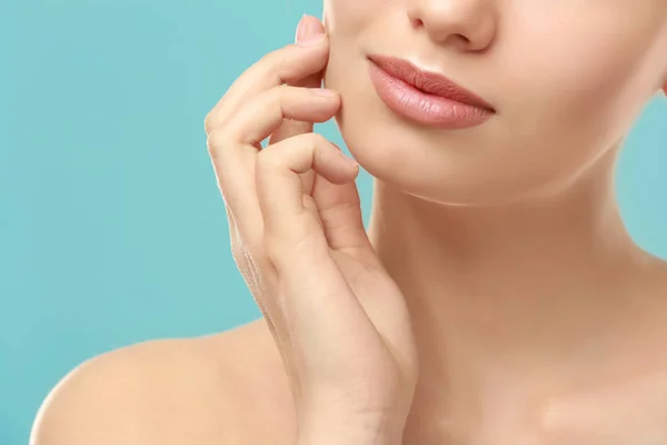 Vista de cerca de la hermosa mujer joven con labios naturales maquillaje tocar la cara en el fondo de color — Foto de Stock