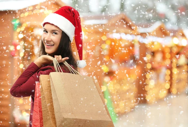 Mujer joven en Santa sombrero con bolsas de compras en la tradicional feria de Navidad. Concepto de Boxeo Día —  Fotos de Stock