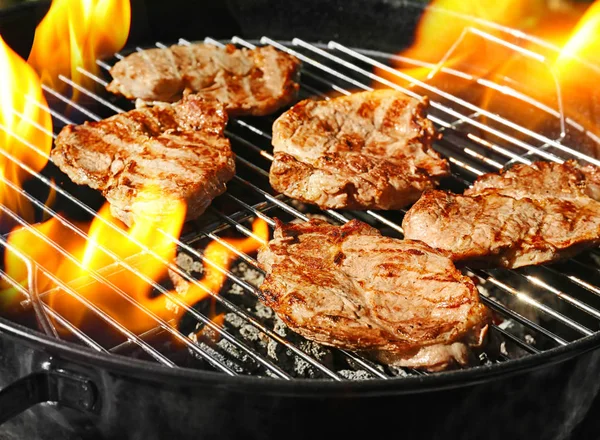 Delicious steaks on grilling grid and flame — Stock Photo, Image
