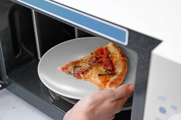 Женщина кладет пиццу в микроволновку — стоковое фото