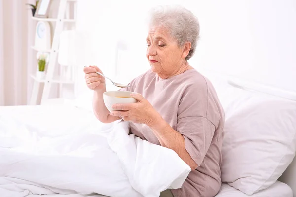 Mujer mayor sentada en la cama y comiendo sopa — Foto de Stock