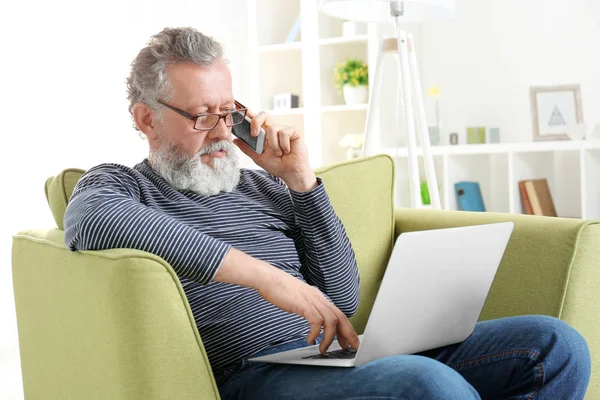 Bonito homem idoso sentado em poltrona com laptop — Fotografia de Stock