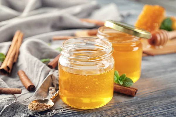 Vasi con miele dorato e cannella sul tavolo di legno — Foto Stock