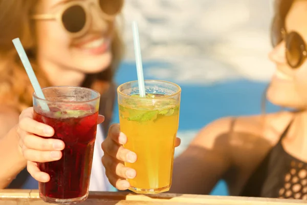 Hermosas mujeres jóvenes tintineo vasos con cócteles mientras se relaja en la piscina, primer plano — Foto de Stock