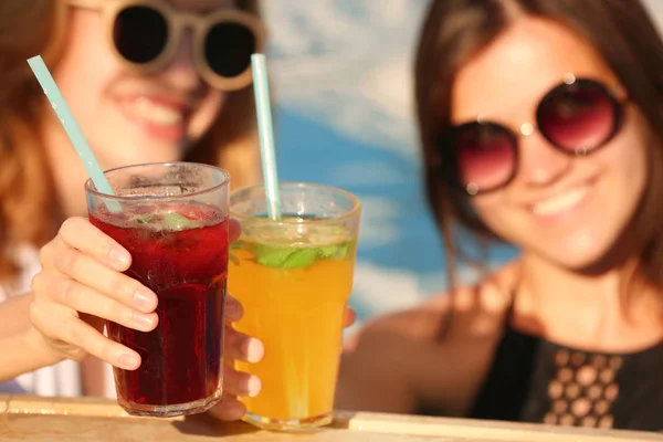 Mooie jonge vrouwen rammelende bril met cocktails terwijl u ontspant in het zwembad, close-up — Stockfoto