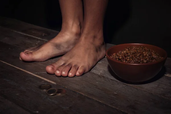 Piedi sporchi di poco, ciotola con lenticchie e monete sul pavimento. Concetto di povertà — Foto Stock