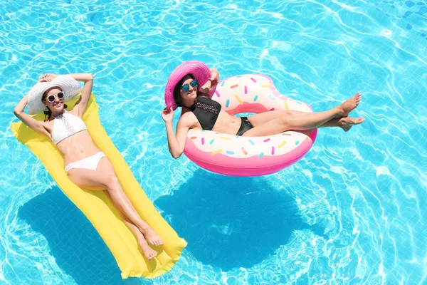 Jovens mulheres bonitas com donut inflável e colchão na piscina azul — Fotografia de Stock