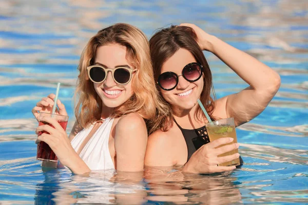 Duas mulheres bonitas com coquetéis relaxantes na piscina — Fotografia de Stock
